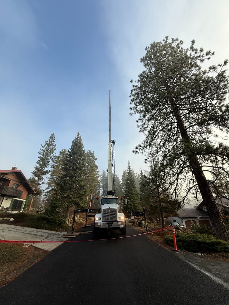 White boom truck with outriggers deployed and boom extended vertically on a residential driveway, caution tape in foreground